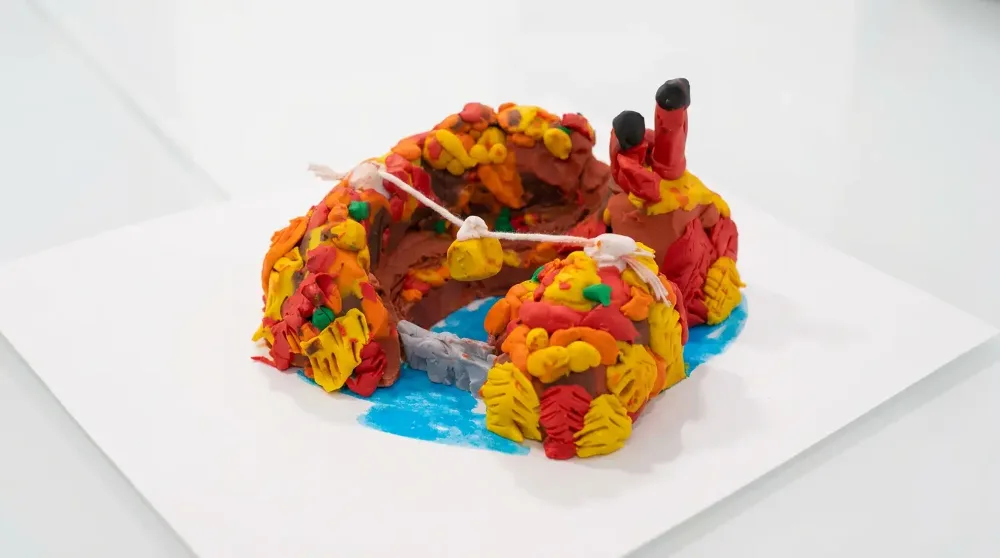 Plasticine model of the Sigulda Autumn Globe – colourful autumn leaves, the Gauja Bridge over the blue river and two chimneys on a white base
