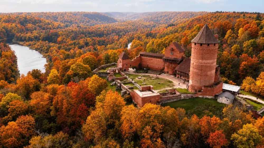 The red-brick tower of Turaida Castle amid the autumn forests of the Gauja valley, seen from above